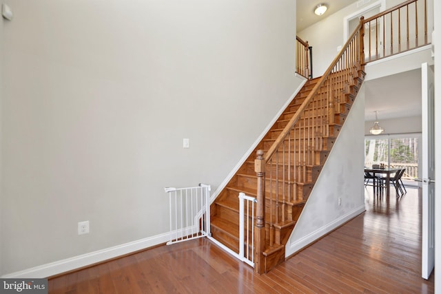 staircase featuring a high ceiling, wood finished floors, and baseboards