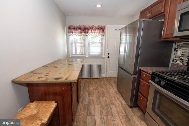 kitchen featuring radiator, butcher block countertops, appliances with stainless steel finishes, wood finished floors, and backsplash