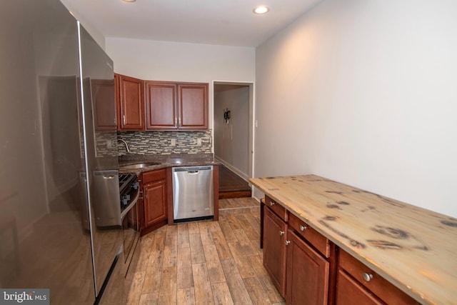 kitchen featuring decorative backsplash, appliances with stainless steel finishes, light wood-style floors, a sink, and wood counters