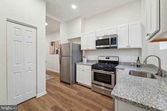 kitchen with sink, light stone counters, stainless steel appliances, light hardwood / wood-style floors, and white cabinets