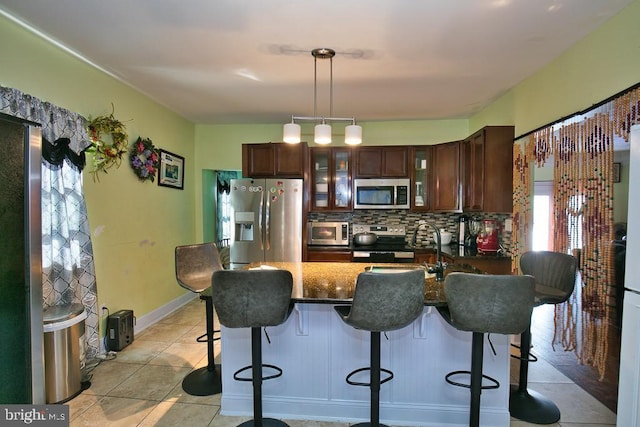 kitchen with light tile patterned floors, tasteful backsplash, glass insert cabinets, a breakfast bar, and stainless steel appliances