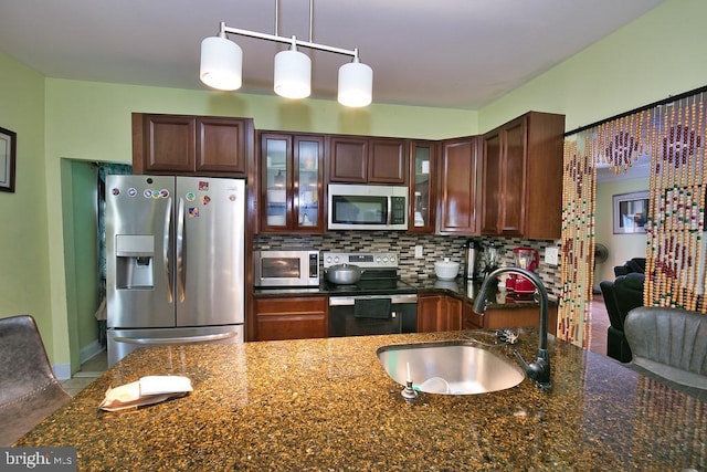 kitchen featuring pendant lighting, tasteful backsplash, appliances with stainless steel finishes, glass insert cabinets, and a sink