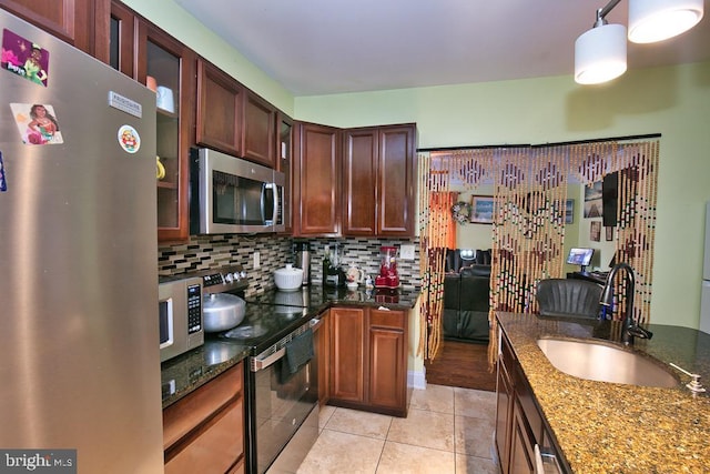 kitchen featuring glass insert cabinets, appliances with stainless steel finishes, dark stone countertops, a sink, and backsplash