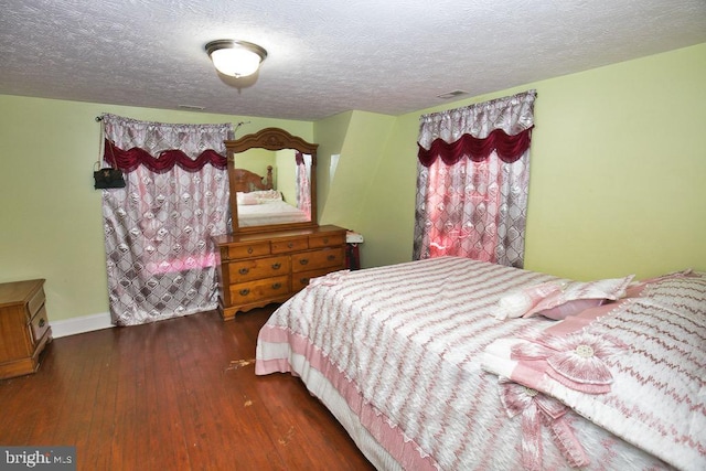 bedroom featuring visible vents, a textured ceiling, baseboards, and wood finished floors