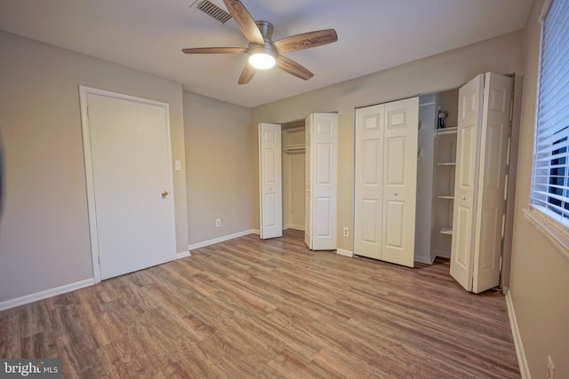 unfurnished bedroom featuring two closets, ceiling fan, and light wood-type flooring