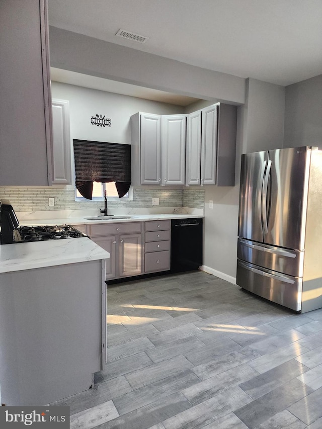 kitchen featuring gray cabinets, black dishwasher, sink, stainless steel fridge, and backsplash