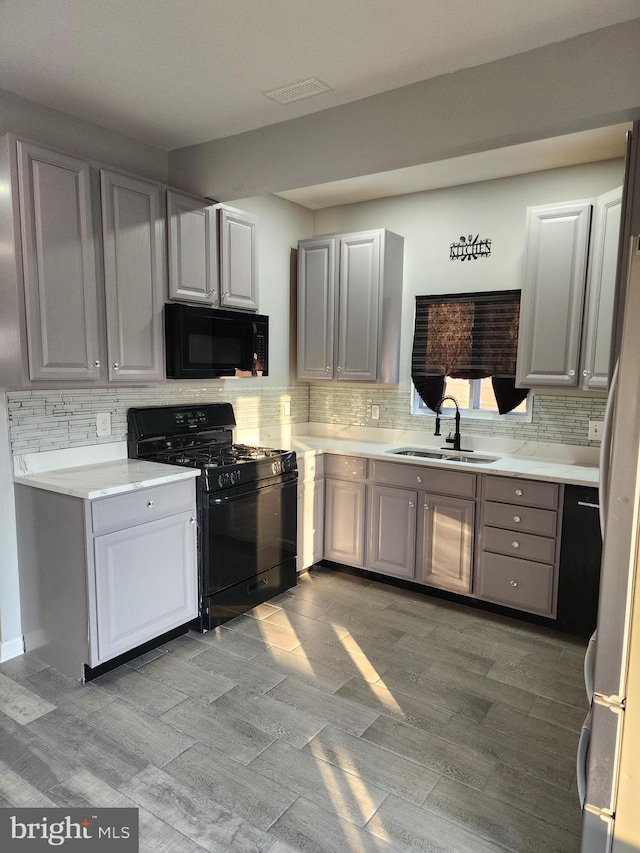 kitchen featuring gray cabinetry, backsplash, sink, and black appliances