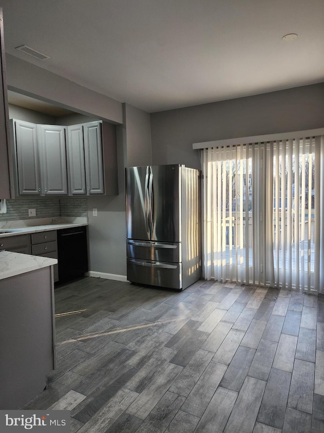 kitchen featuring gray cabinetry, stainless steel refrigerator, dark hardwood / wood-style floors, black dishwasher, and backsplash