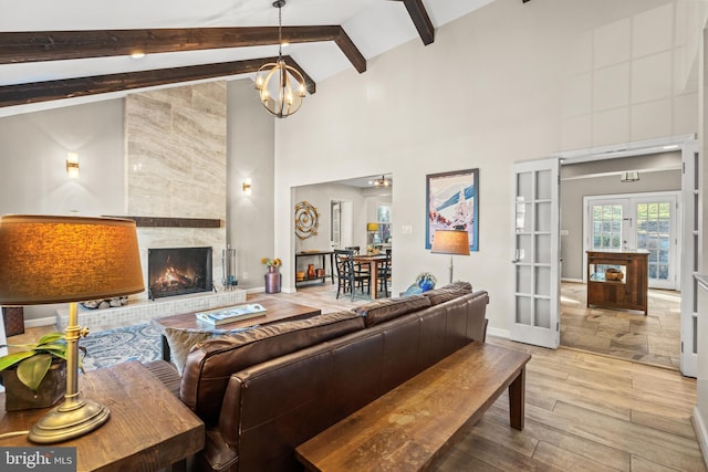 living room featuring french doors, high vaulted ceiling, light hardwood / wood-style flooring, beamed ceiling, and a tiled fireplace