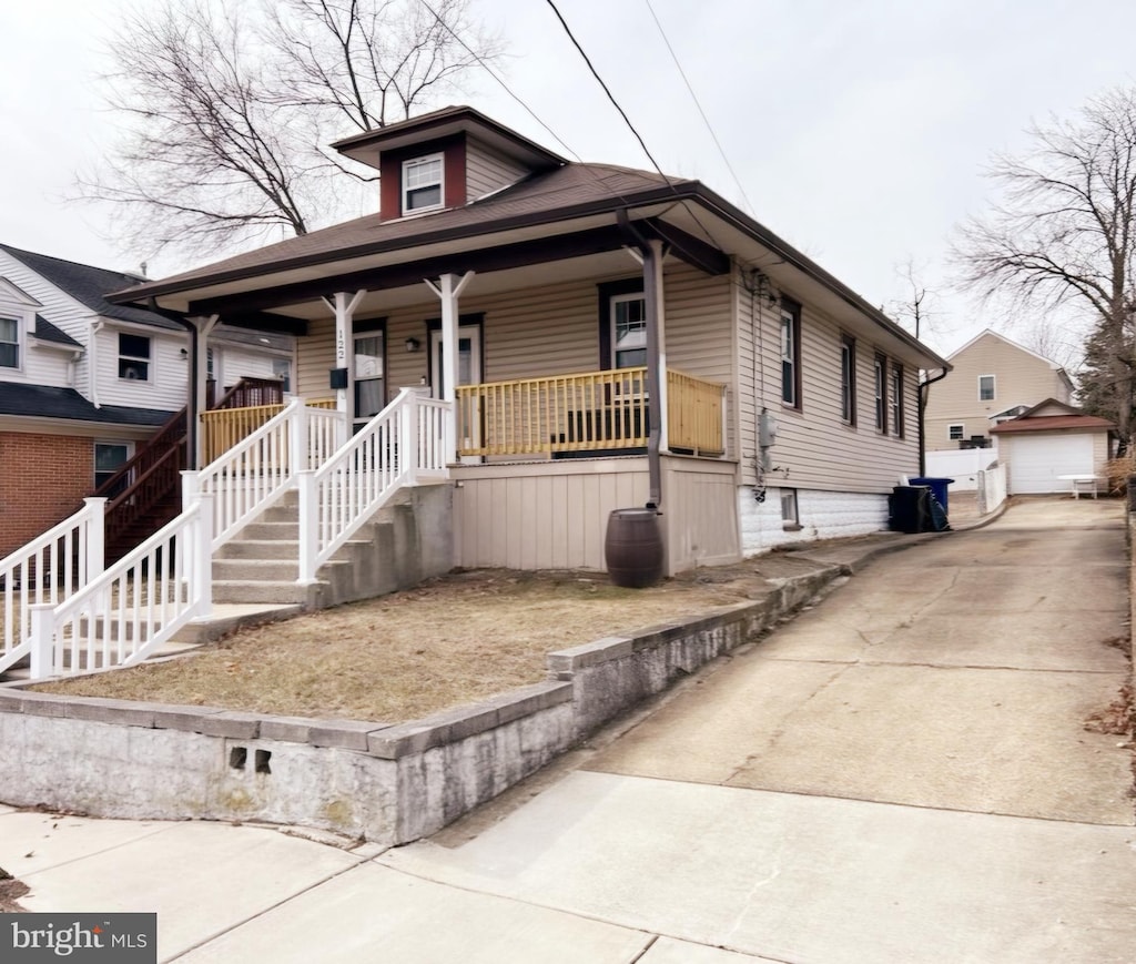 bungalow-style house with a garage, a porch, concrete driveway, and an outbuilding