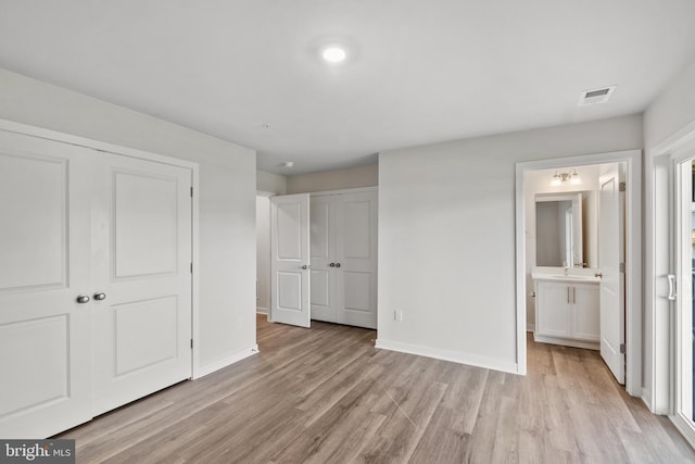 unfurnished bedroom featuring sink, light wood-type flooring, and ensuite bath