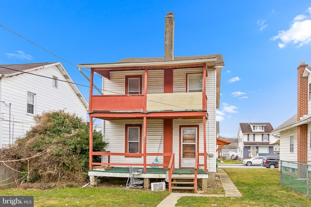 rear view of house featuring a lawn, a balcony, and covered porch