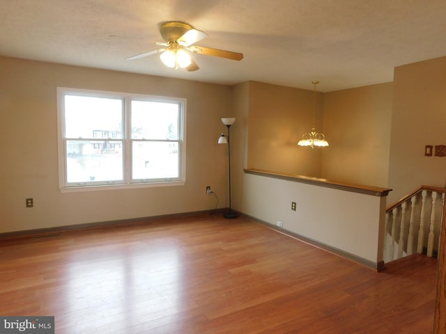 empty room featuring ceiling fan with notable chandelier and light hardwood / wood-style floors