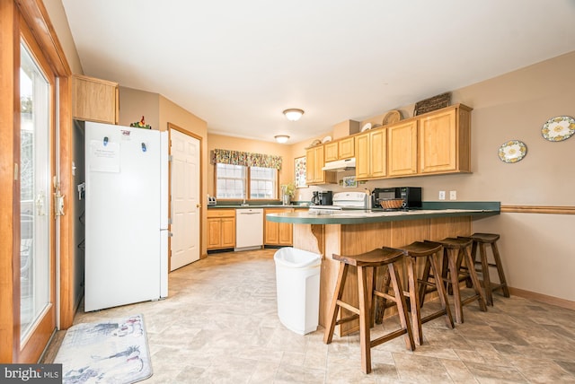 kitchen with a kitchen bar, white appliances, kitchen peninsula, and light brown cabinets