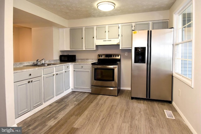 kitchen featuring under cabinet range hood, plenty of natural light, appliances with stainless steel finishes, and wood finished floors