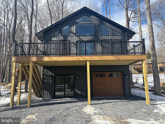 chalet / cabin with a garage, board and batten siding, gravel driveway, and a wooden deck