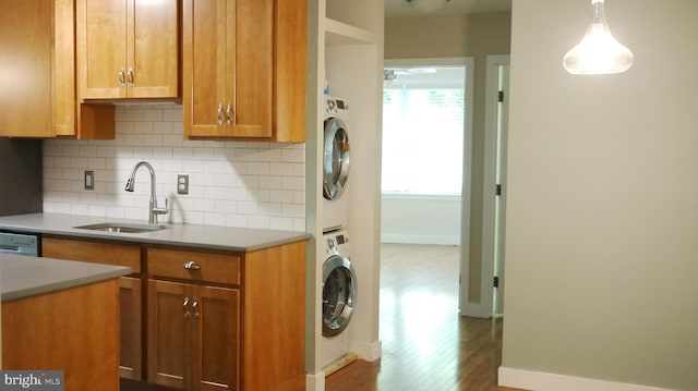 kitchen featuring stacked washer and clothes dryer, sink, tasteful backsplash, dark hardwood / wood-style flooring, and pendant lighting