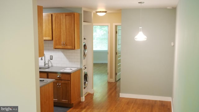 kitchen featuring sink, decorative light fixtures, stacked washing maching and dryer, light hardwood / wood-style floors, and decorative backsplash