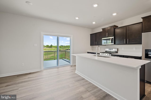 kitchen featuring appliances with stainless steel finishes, an island with sink, sink, dark brown cabinetry, and light hardwood / wood-style floors