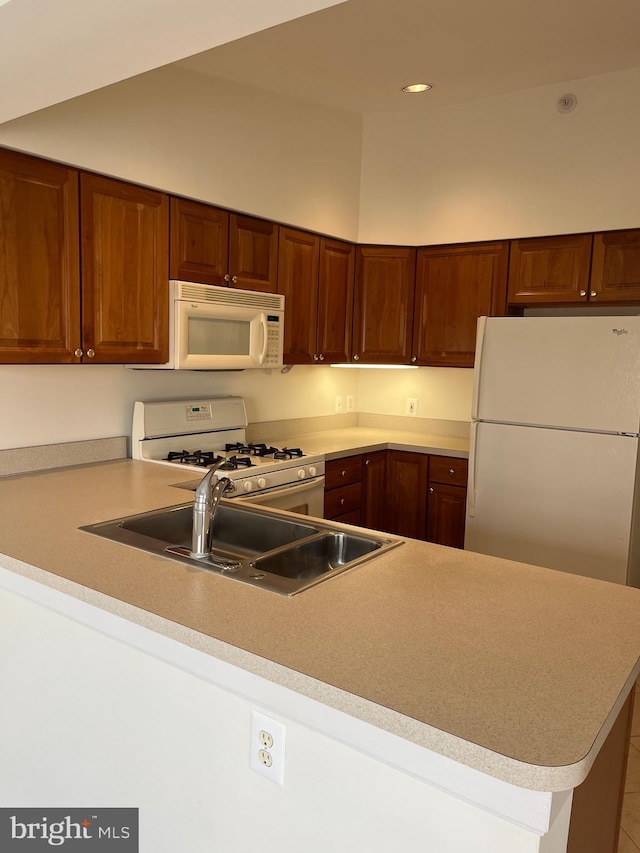 kitchen featuring white appliances, kitchen peninsula, and sink