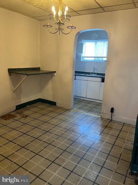 unfurnished dining area with an inviting chandelier, dark tile patterned flooring, sink, and a drop ceiling