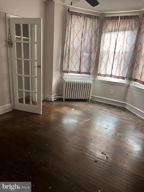 unfurnished room with dark hardwood / wood-style flooring, radiator, and ceiling fan