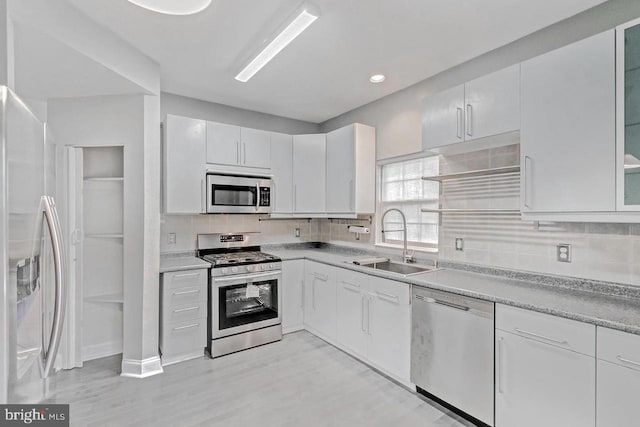 kitchen featuring sink, white cabinetry, appliances with stainless steel finishes, light hardwood / wood-style floors, and backsplash