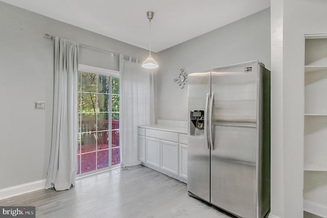 kitchen featuring white cabinets, light hardwood / wood-style flooring, stainless steel fridge, and decorative light fixtures