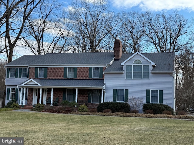 traditional-style house with roof with shingles, a front lawn, a chimney, and brick siding