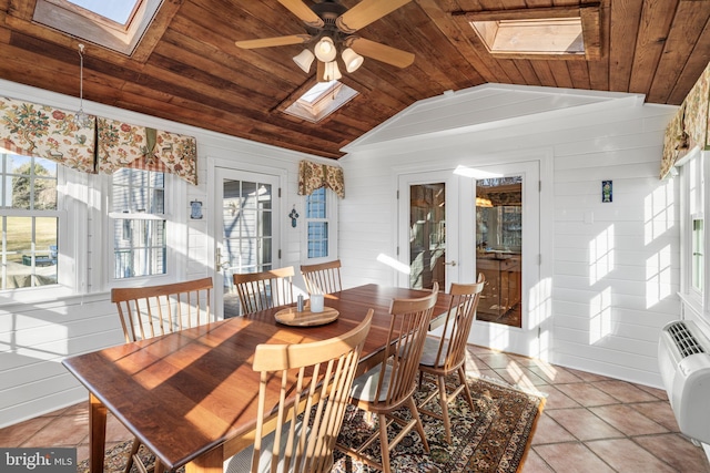 dining room with light tile patterned floors, vaulted ceiling with skylight, a ceiling fan, wood ceiling, and wood walls