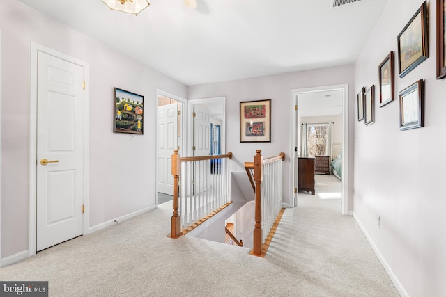 hallway with baseboards, an upstairs landing, and light colored carpet