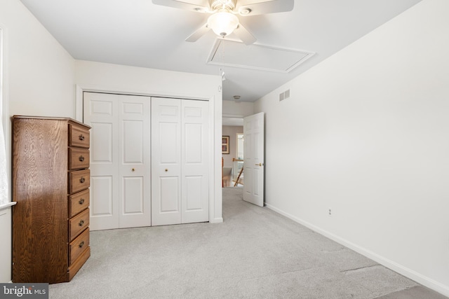 unfurnished bedroom with attic access, baseboards, light colored carpet, ceiling fan, and a closet