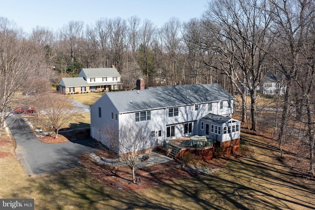 view of front of house with a sunroom, driveway, a chimney, and a front lawn