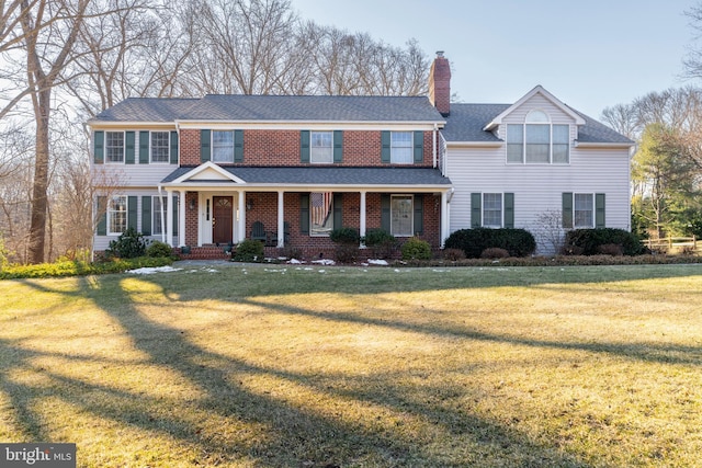 view of front of home featuring covered porch, a chimney, brick siding, and a front yard