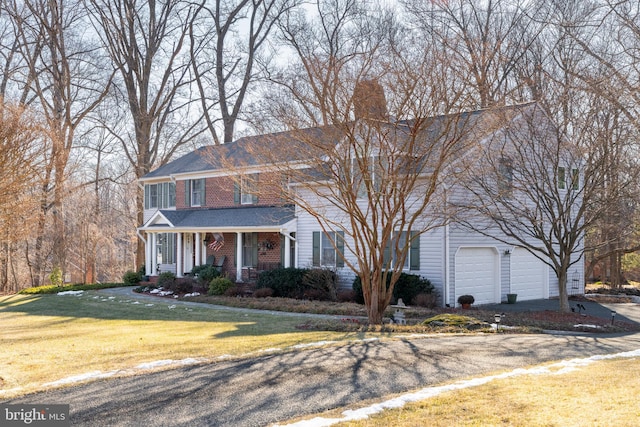 colonial inspired home featuring aphalt driveway, covered porch, a garage, brick siding, and a front lawn