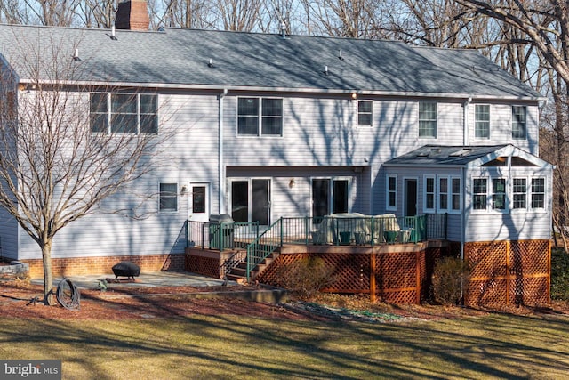 back of house featuring a shingled roof, a chimney, a lawn, and a wooden deck