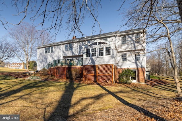 rear view of house with a chimney, brick siding, a lawn, and a deck