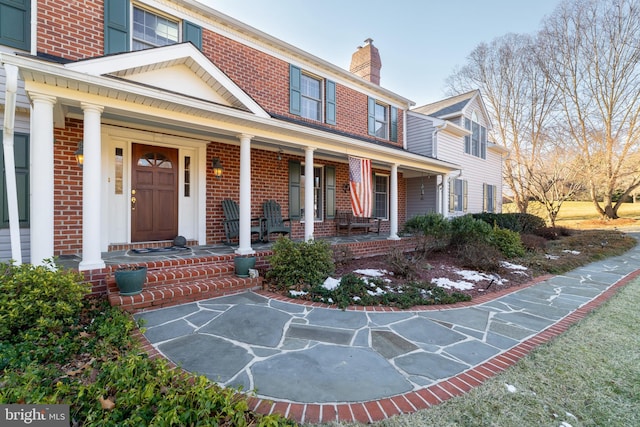 view of exterior entry with covered porch, brick siding, and a chimney