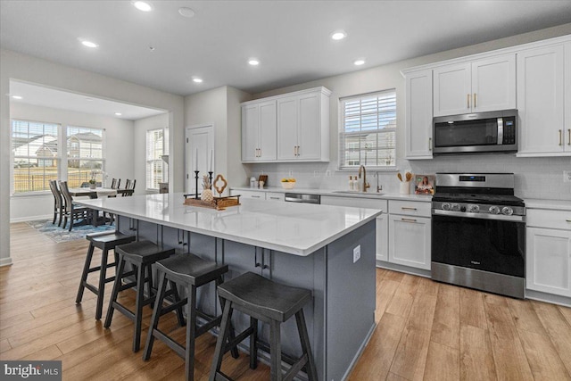 kitchen with appliances with stainless steel finishes, white cabinetry, a kitchen breakfast bar, a center island, and light hardwood / wood-style floors