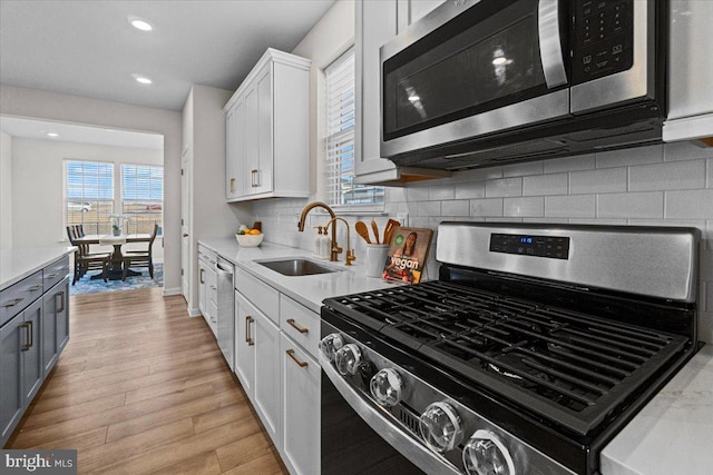 kitchen with sink, white cabinetry, appliances with stainless steel finishes, light hardwood / wood-style floors, and backsplash