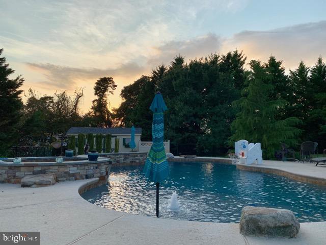 pool at dusk featuring a patio area and pool water feature