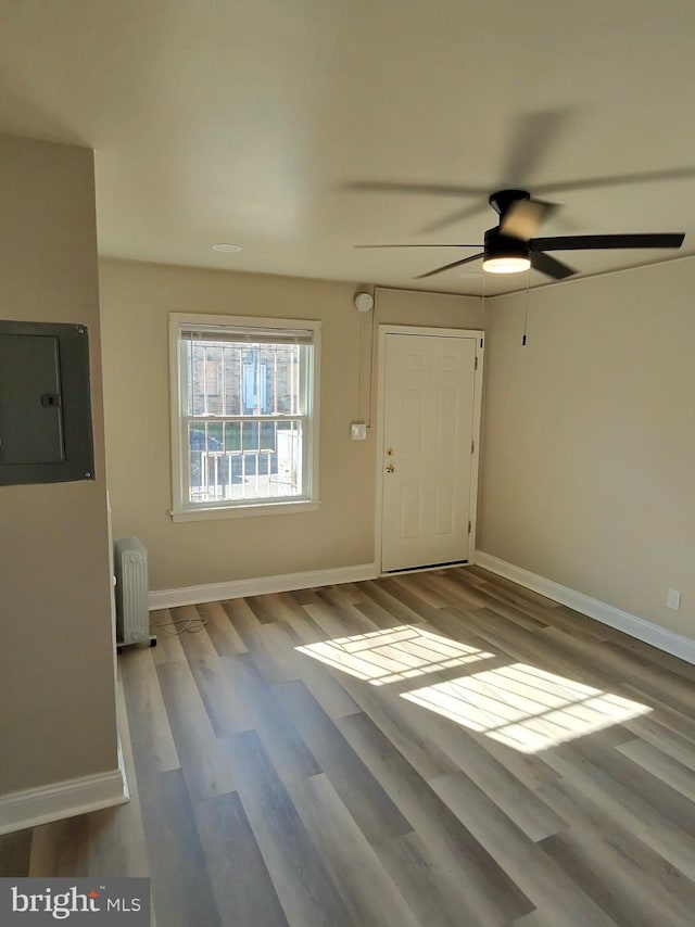 interior space featuring ceiling fan, radiator heating unit, electric panel, and hardwood / wood-style floors