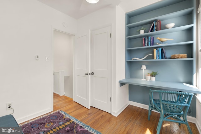 home office featuring built in desk, built in shelves, baseboards, and wood finished floors