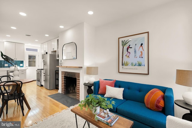 living room featuring light wood-style floors, recessed lighting, and a brick fireplace