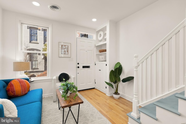 living area with stairway, wood finished floors, visible vents, and a healthy amount of sunlight