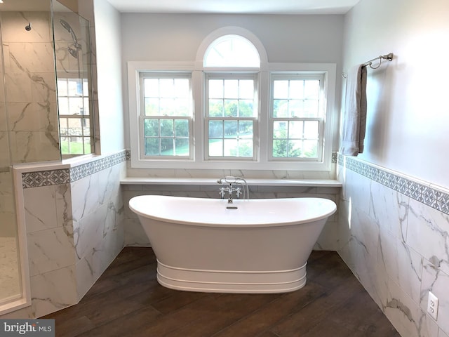 bathroom with a freestanding tub, tile walls, wood finished floors, and wainscoting