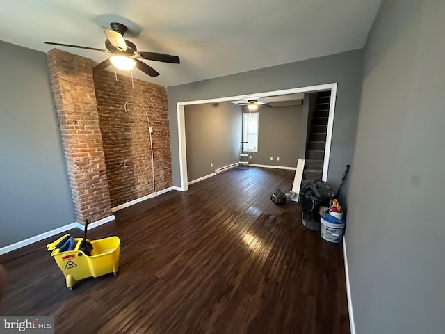 unfurnished room with dark hardwood / wood-style floors, ceiling fan, and brick wall