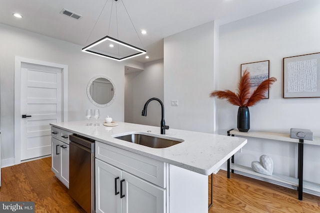 kitchen with sink, decorative light fixtures, dishwasher, light stone countertops, and a kitchen island with sink