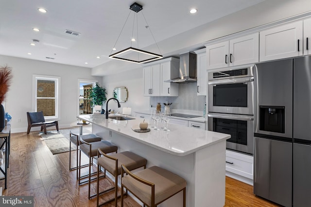 kitchen with stainless steel appliances, an island with sink, white cabinetry, and wall chimney exhaust hood