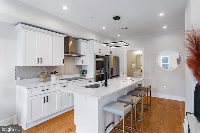 kitchen featuring white cabinets, sink, wall chimney range hood, and a kitchen island with sink